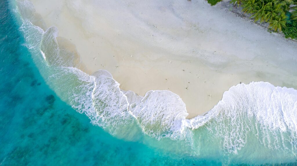Aerial view of turquoise waves washing onto a white sand beach on a Maldives local island