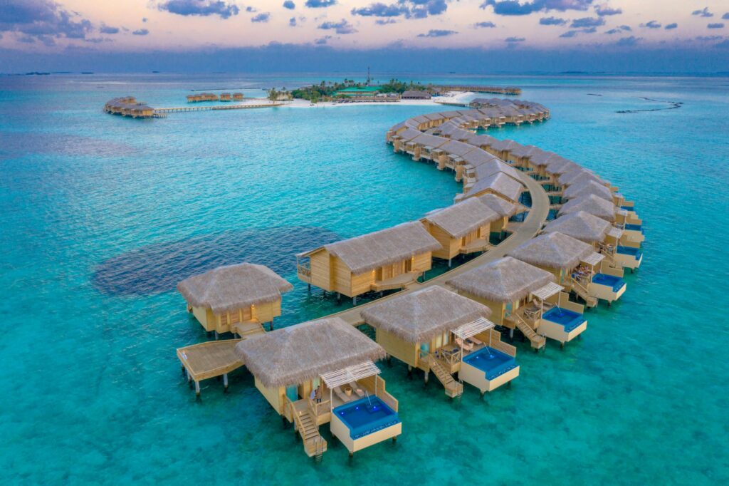 Aerial view of luxury overwater bungalows with private pools at a Maldives resort island.