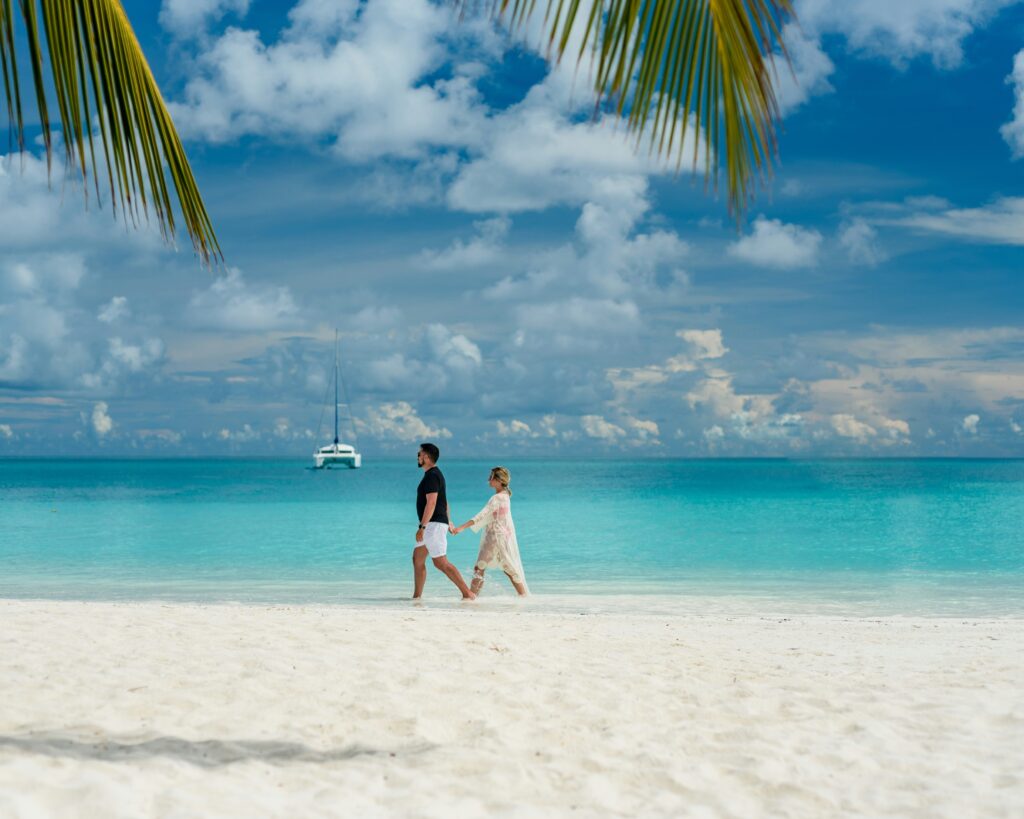 Couple walking hand in hand on a white sand Maldives beach with turquoise water and palm trees.