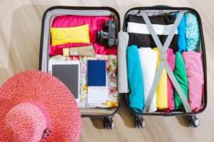 Open suitcase packed with clothes, sunscreen, camera, passport and sun hat for a Maldives trip.