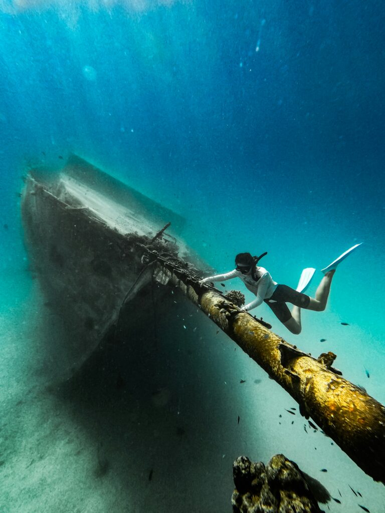 Freediver exploring sunken shipwreck on ocean floor at Maldives wreck dive site.